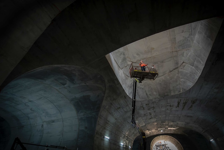 A worker on a forklift is raised up into a cavernous underground tunnel