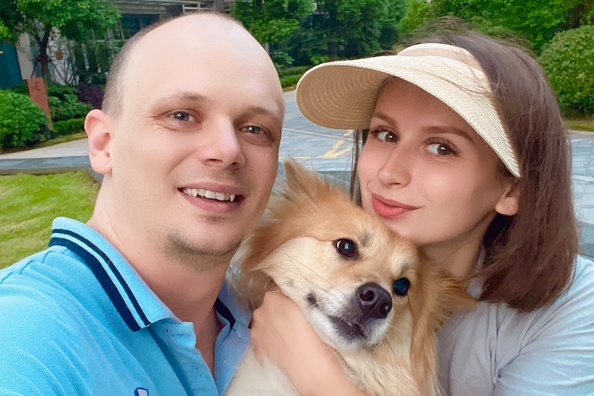 a man and a woman smile at the camera in a selfie, holding their dog