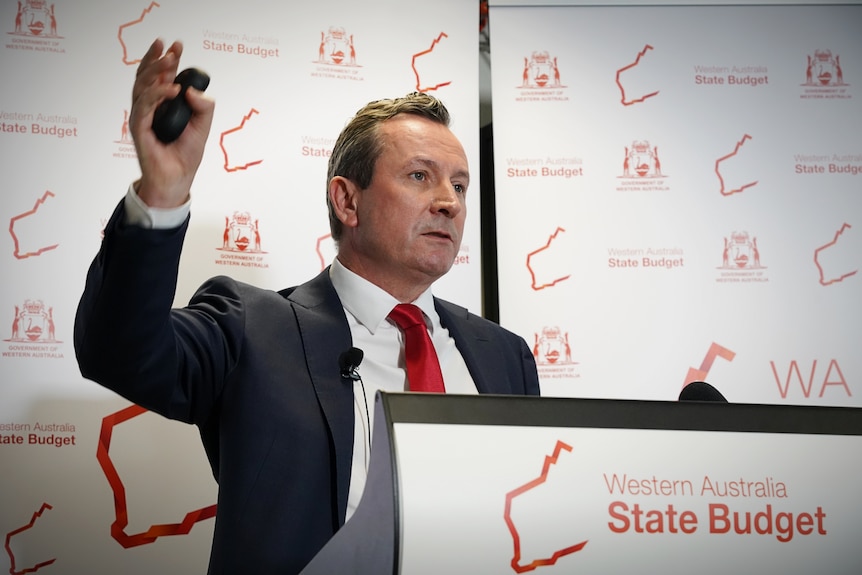 A man in a suit and red tie delivers a powerpoint presentation