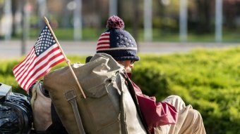 A homeless man with a US flag attached to his backpack.