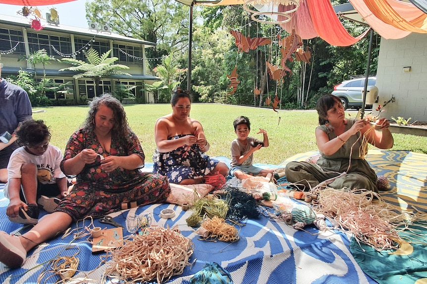 People sitting on a mat weaving with raffia