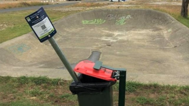 COVID check-in QR code signage near skate park bin.