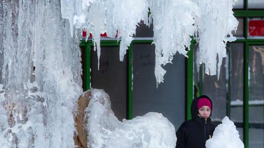A woman passes an ice-covered fountain in New York