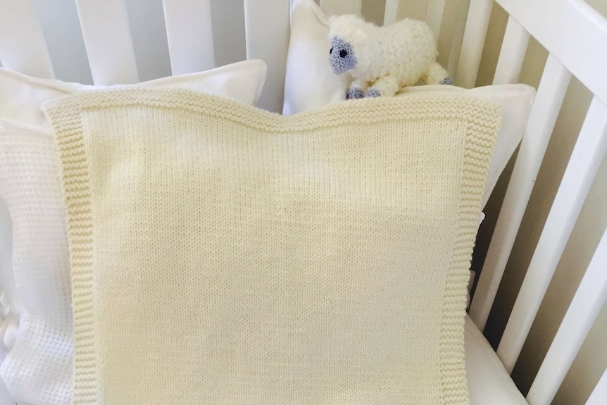 A hand-knitted wool baby blanket in a cot.
