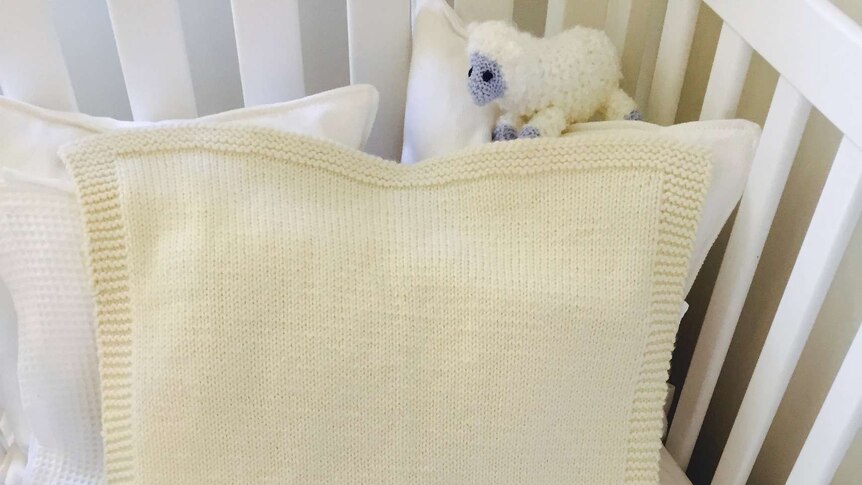 A hand-knitted wool baby blanket in a cot.