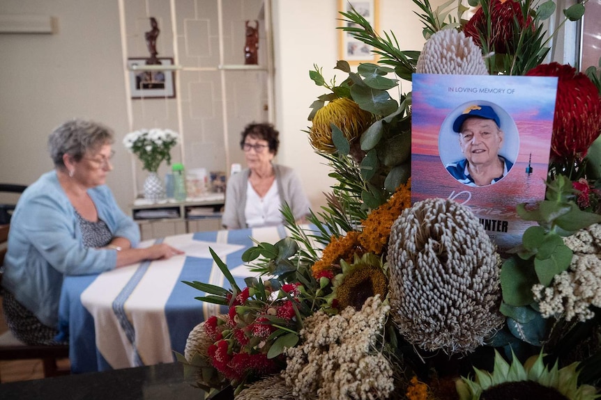 Two women sit in front of memorial flowers.