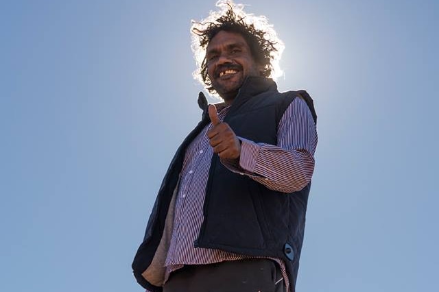 A man smiling at the camera with his thumbs up