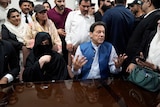 Bushra Bibi sits next to Imran Khan who are both behind a table surrounded by people at a press conference