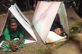 Two people lying in triangular huts made from plastic boards.