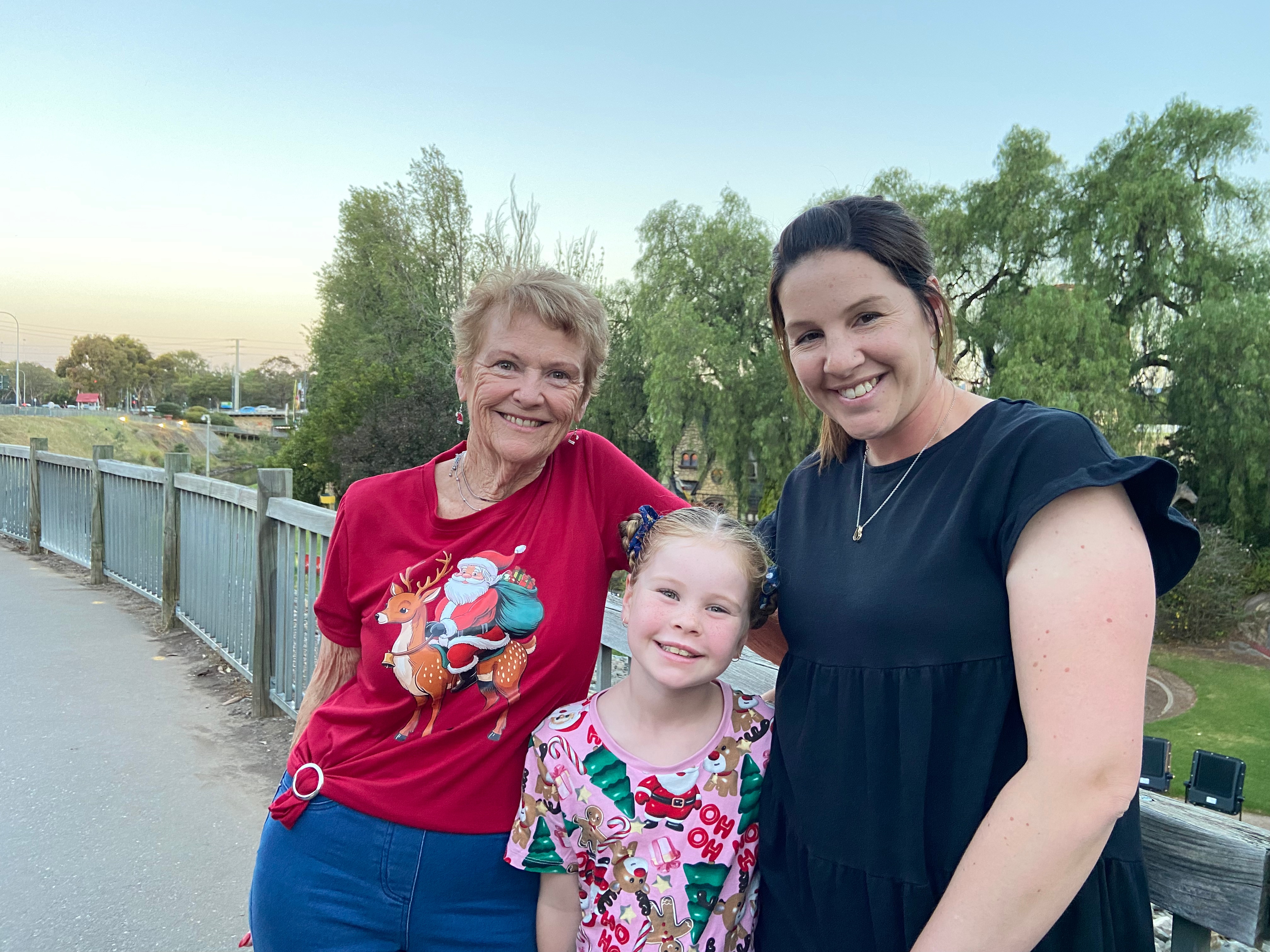 Una hija, una madre y una abuela sonríen a la cámara en un puente antes de un espectáculo navideño junto al río