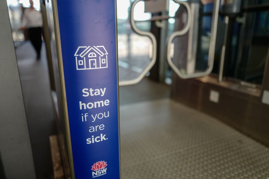Blue NSW Government sign at train station reads: "Stay home if you are sick."