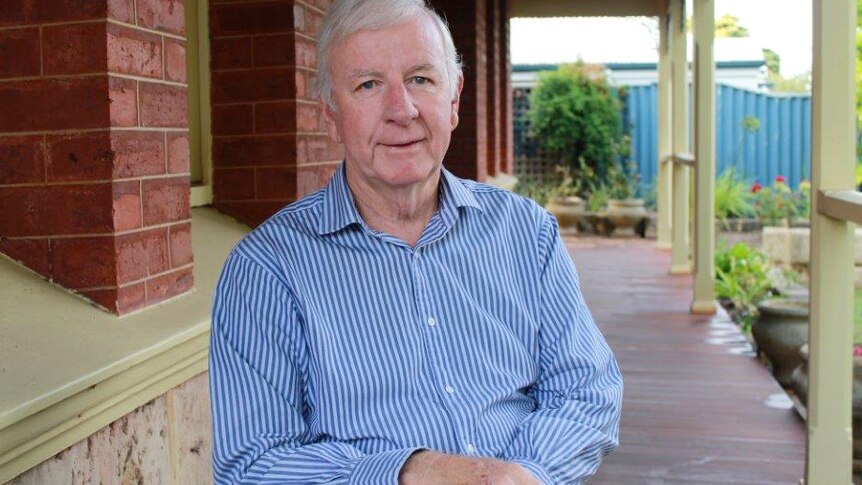 Jim McGinty poses for the camera on a verandah in a blue and white striped shirt.