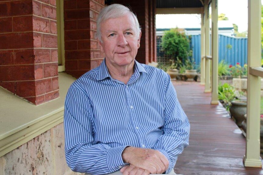 Jim McGinty poses for the camera on a verandah in a blue and white striped shirt.