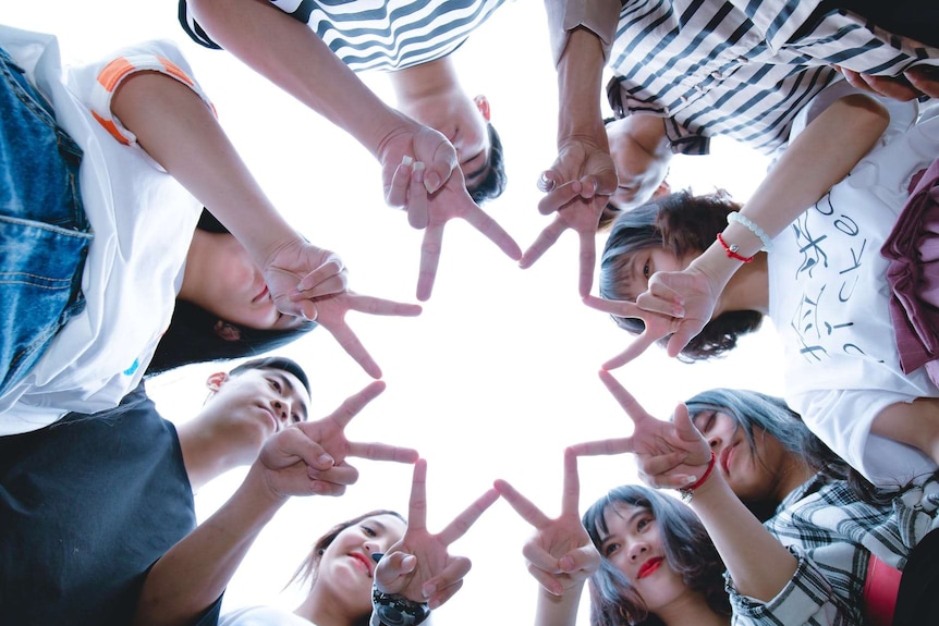 A group of people shot from below holding their fingers in the shape of a star.