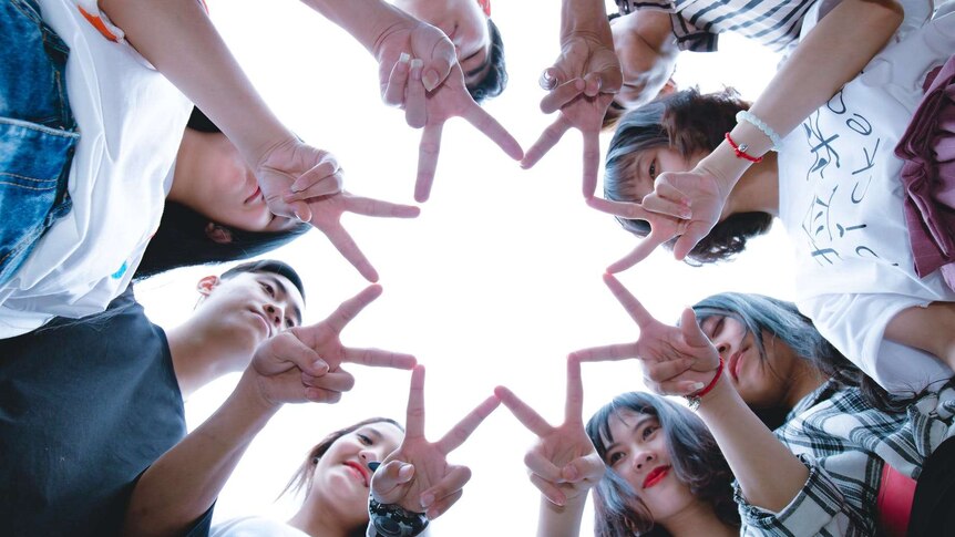 A group of people shot from below holding their fingers in the shape of a star.