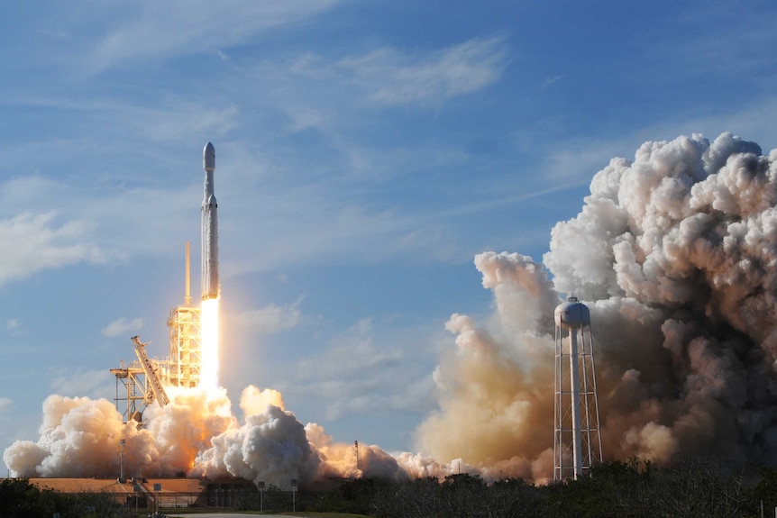 The SpaceX Falcon Heavy rocket launches in a cloud of smoke.