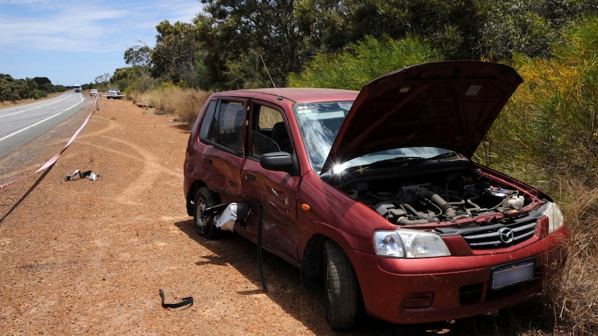 A damaged car by the side of a road.