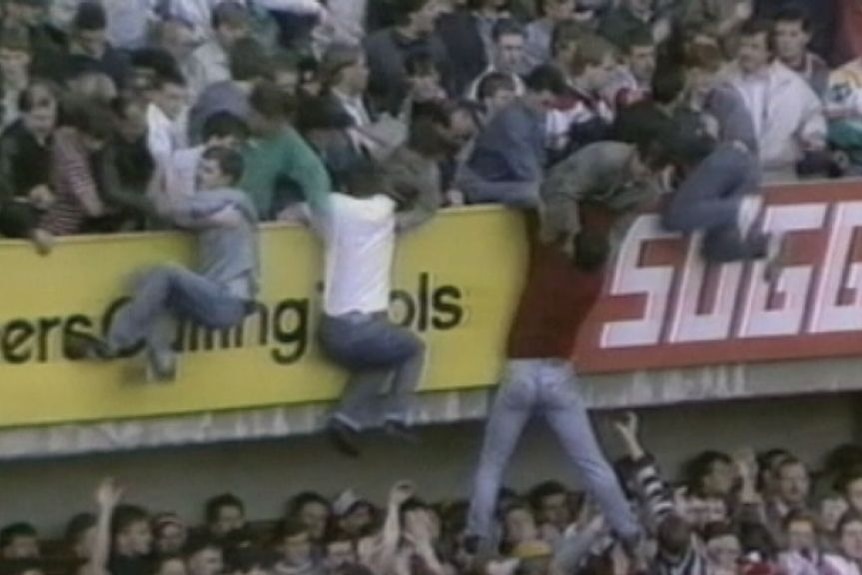 Archival footage from the Hillsborough stadium crush shows fans dangling over barricades trying to hold on to friends.