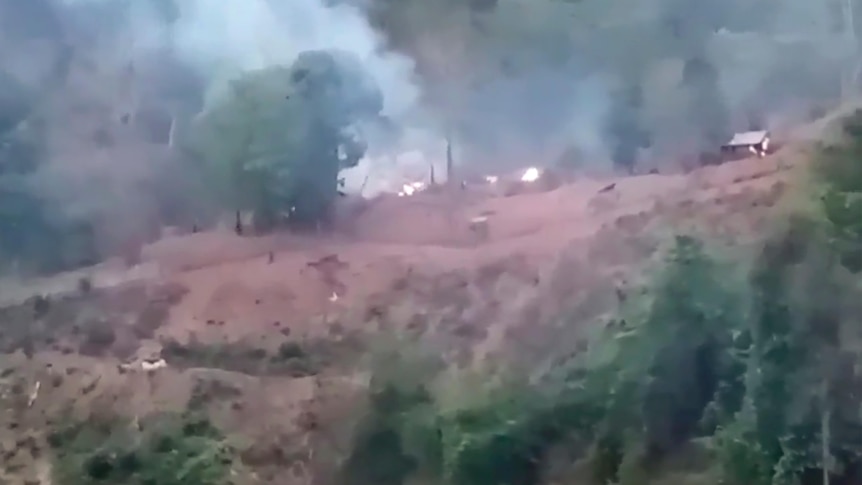 Smoke rises from a hilltop camp in a grainy image