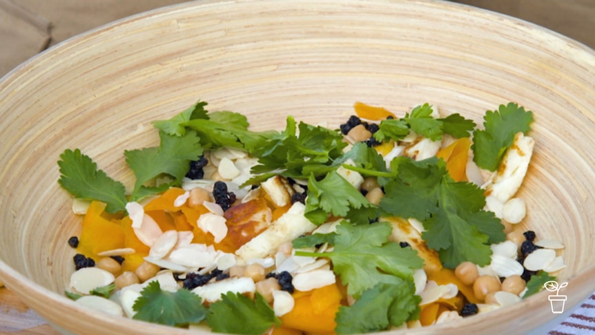 Wooden bowl filled with leafy greens, pumpkin and chickpeas