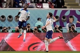 An England footballer leaps high in the air in celebration after scoring a World Cup goal as his teammate punches the air.