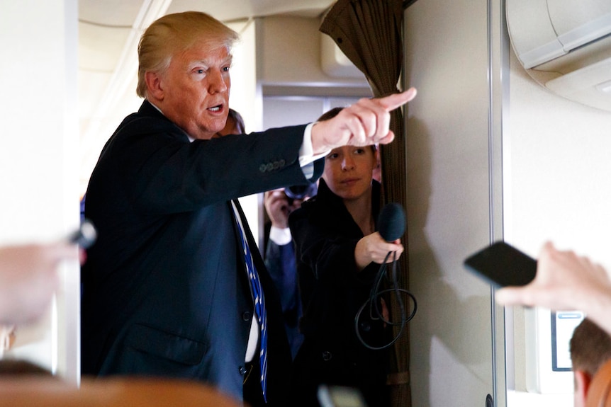 US President Donald Trump points as he speaks with reporters on Air Force One.