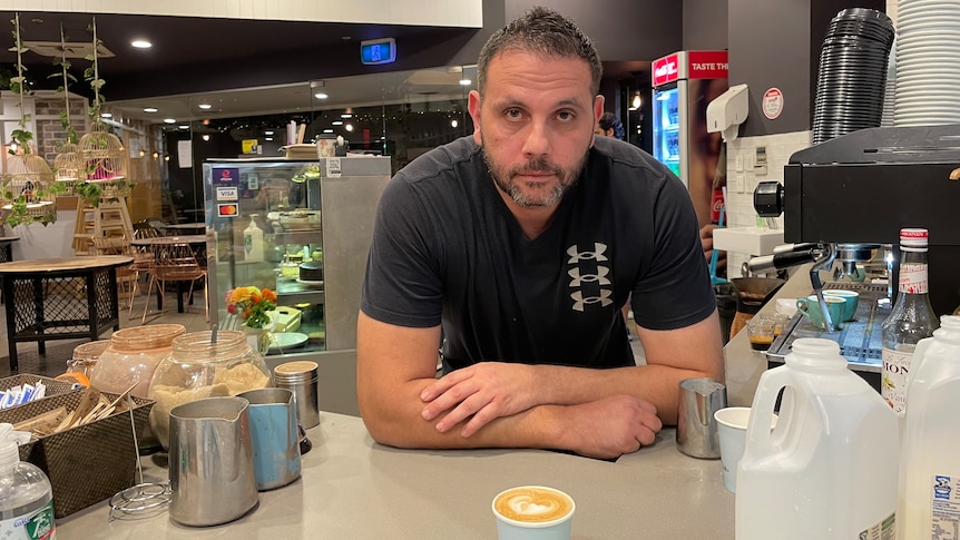 Bankstown cafe owner Izzat Khatib leaning over the counter of his cafe with his arms crossed.