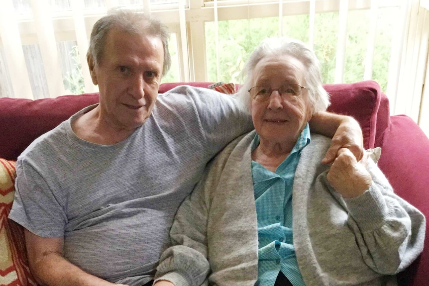 A man in his 60s and his elderly mother smile while seated for a photo