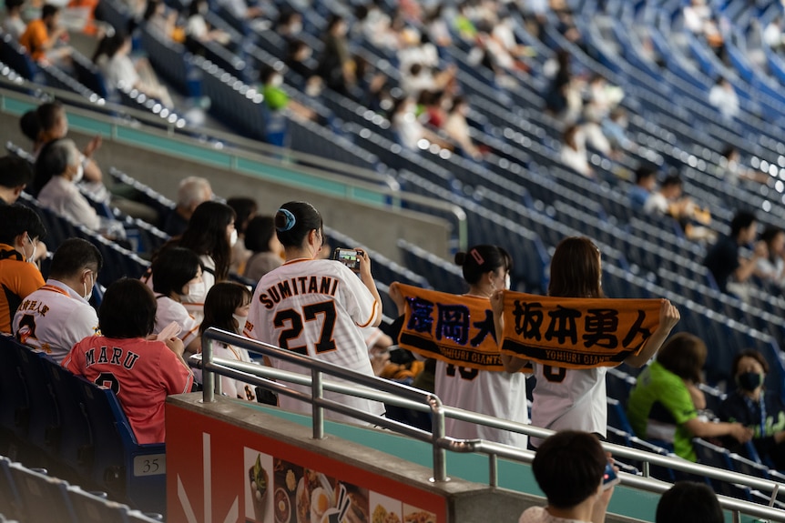 Girls in baseball jerseys hold up banners in a stadium 