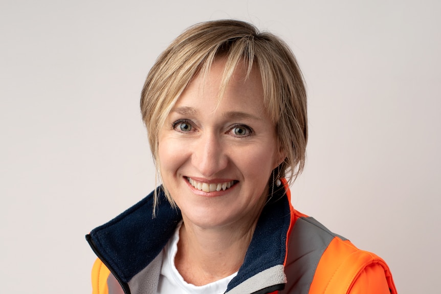 Woman with short blonde hair wearing high vis smiles at Camera 