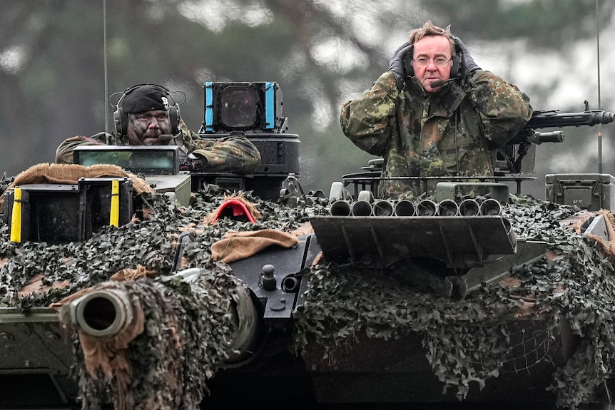German Defense Minister Boris Pistorius blocks his ears as he looks out from a Leopard 2 tank.