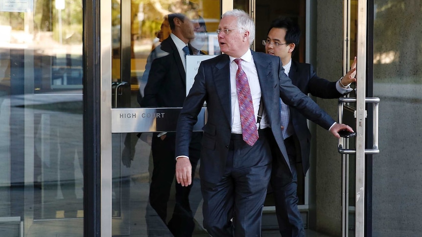 Bret Walker SC walks out a glass door at the High Court, with a phone in his leave hand.