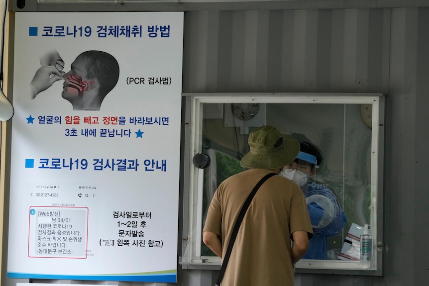 A medical worker in a booth takes a nasal sample from a man at a coronavirus testing site in Seoul.