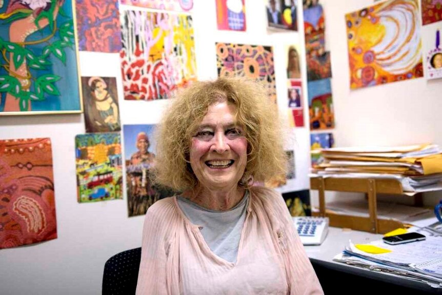 Ms Buchanan sits in an office smiling, there is Aboriginal art on the walls behind her.