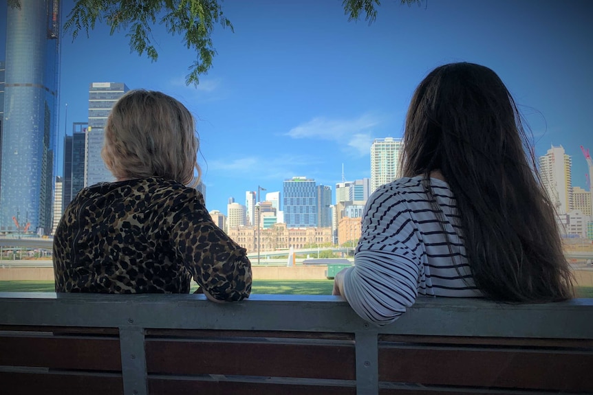 Two women sit on a park bench looking at the London skyline