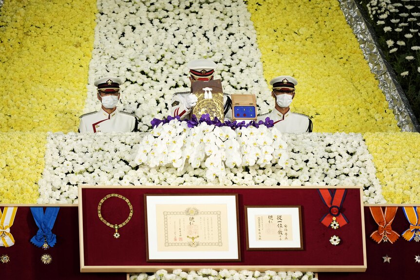 Honour guards place a cinerary urn on an altar during a large state funeral.