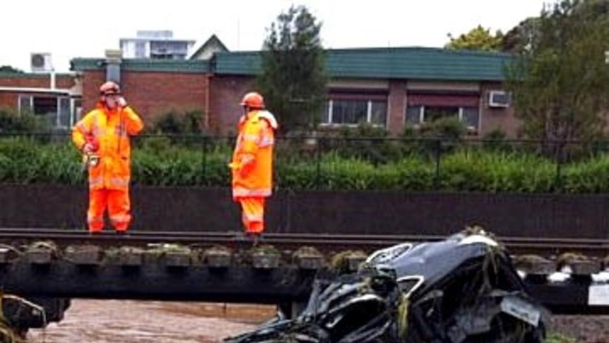 Emergency services workers look at the wrecks of two cars sitting against a rail bridge in Toowoomba