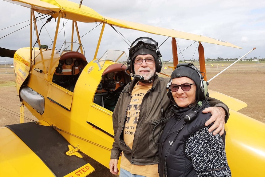 a man and woman with flying helmets stand next to an old yellow plane