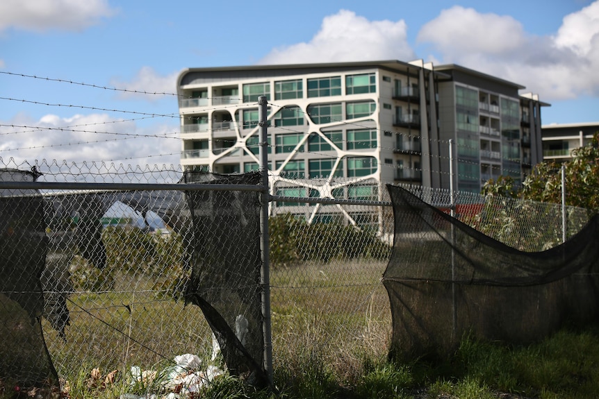 A block of flats in the background with a barbed wire fence in the foreground. 