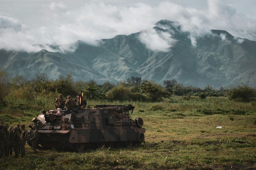 A tank sits near a mountain on a barren field.