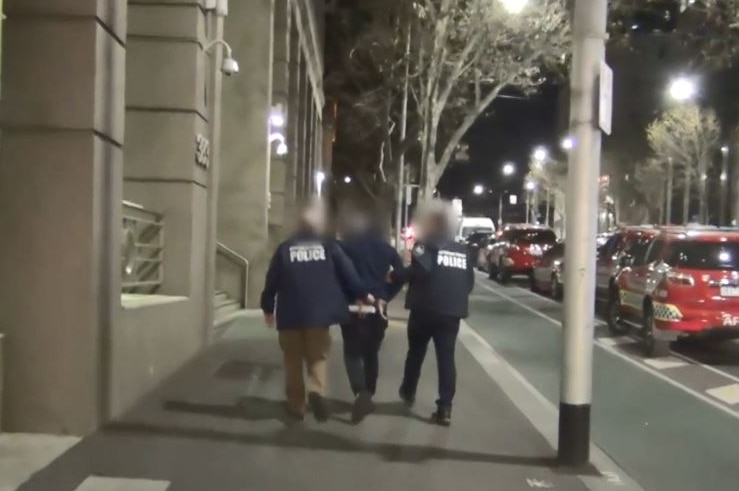 Two police escort an arrest man along a city street at night.