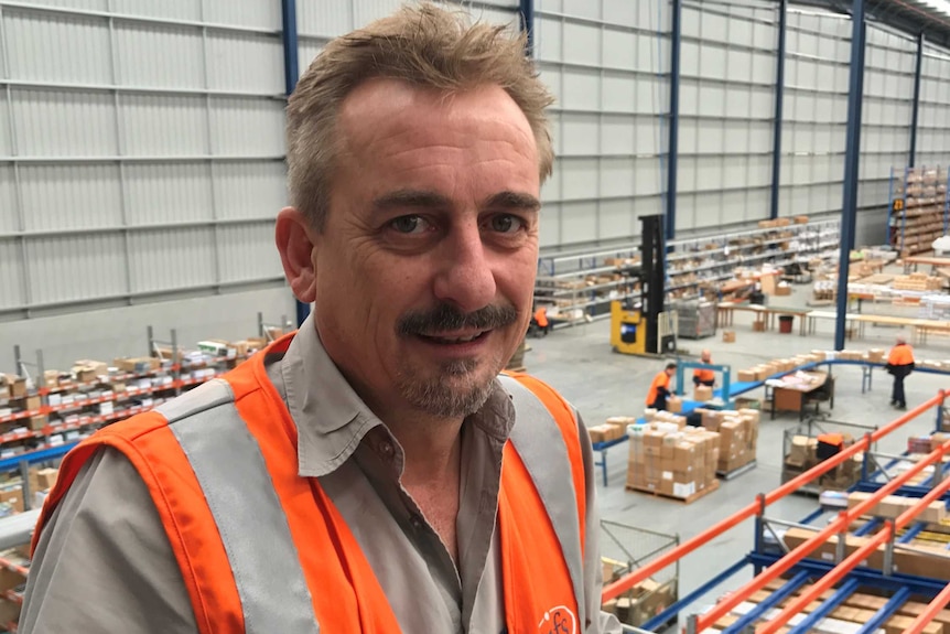 A man in a hi-vis vest in a warehouse filled with boxes
