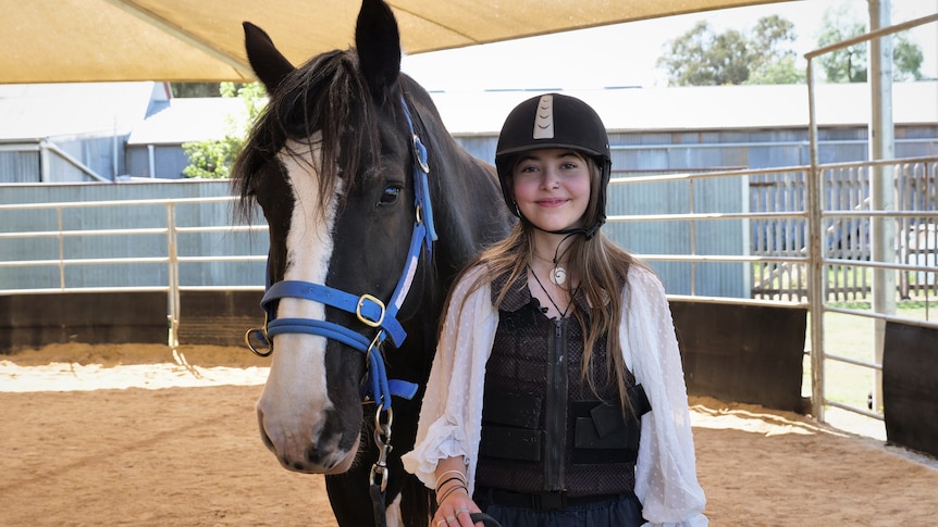 Jade wears a helmet and safety vest while holding Queenie, who has a blue halter. 