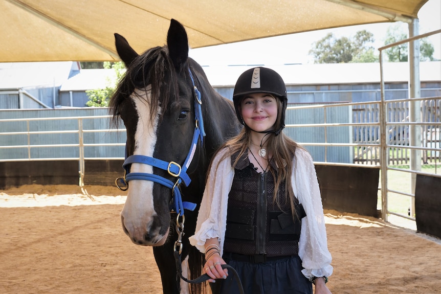 Jade wears a helmet and safety vest while holding Queenie, who has a blue halter. 