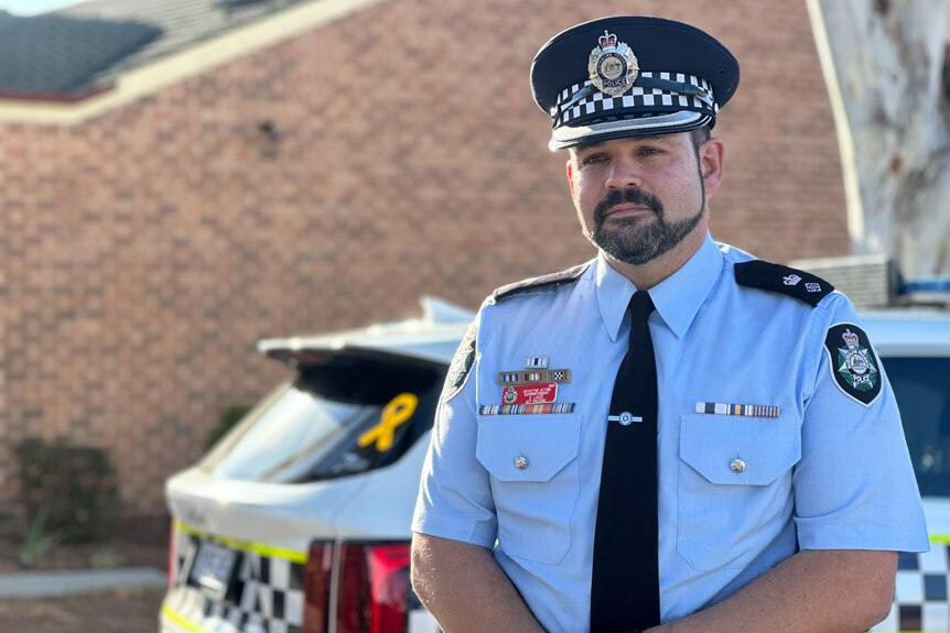 Detective Acting Superintendent Stephen Ladd wearing police uniform and standing in front of a police car.