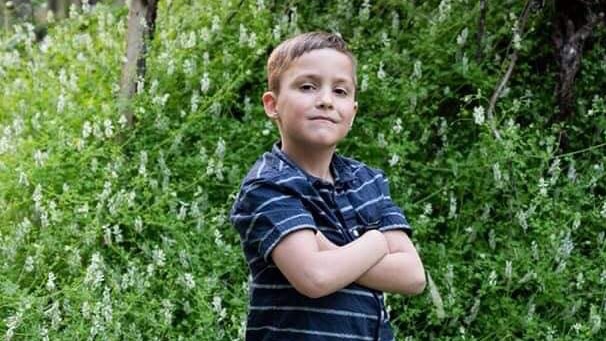 A boy stands in the garden arms crossed