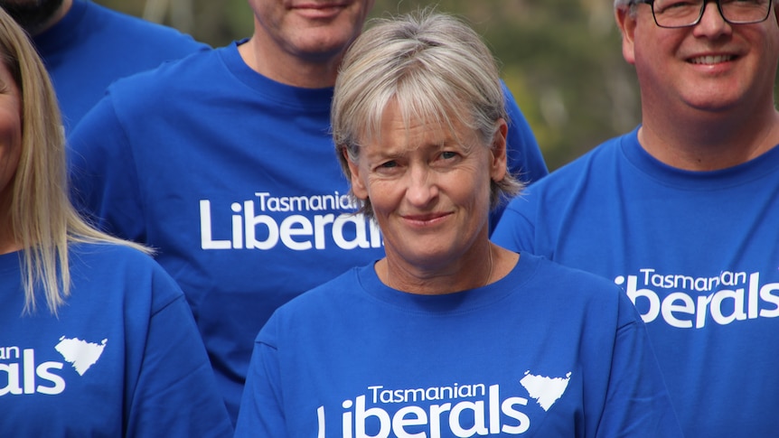 A woman with short silver hair and a blue t-shirt reading Tasmanian Liberals stands amongst others in blue t-shirts.