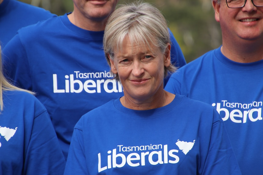 A woman with short silver hair and a blue t-shirt reading Tasmanian Liberals stands amongst others in blue t-shirts.