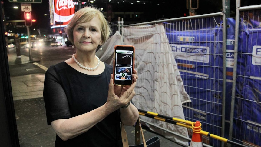 A woman standing in front of a construction site with an app on her phone to monitor noise.