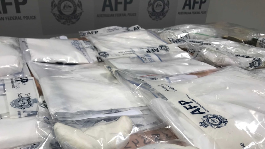 Bags of white packages with the Australian Federal Police logo are arranged on a table.